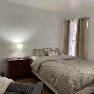 A cozy bedroom with a neatly made bed, a nightstand with a lamp, and curtains by the window.