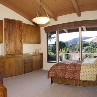 A cozy bedroom featuring wooden furniture and large windows with a scenic view.