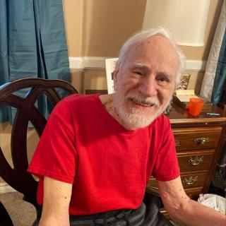 An elderly man smiling while seated indoors.