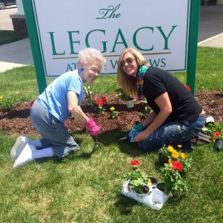 Two people gardening together in front of a sign that says 'The Legacy'.
