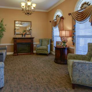 A traditional living room with elegant furnishings, featuring armchairs, a fireplace, and decorative curtains.