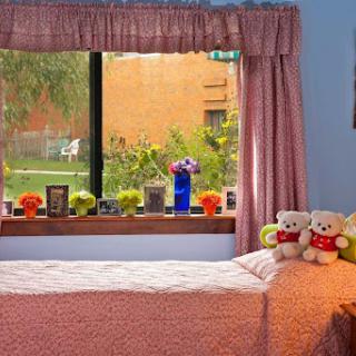 A cozy bedroom featuring a plush bed, cheerful stuffed animals, and a bright window adorned with flowers.