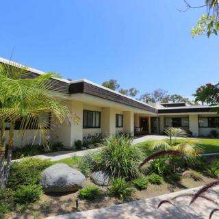 A modern single-story house with well-maintained landscaping and palm trees under a clear blue sky.