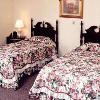 A cozy bedroom with two twin beds featuring floral bedding, a bedside lamp, and a painting on the wall.