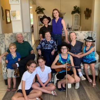A family group photo featuring multiple generations, with members sitting and standing in a cozy living room.