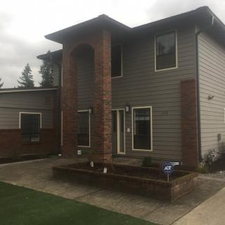 A two-story house with grey siding and brick accents on an overcast day.
