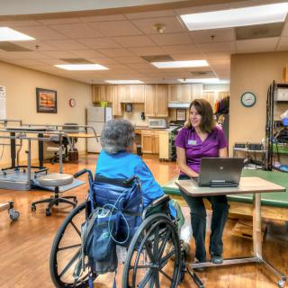 A therapist engages with a patient in a wheelchair during a rehabilitation session in a healthcare facility.
