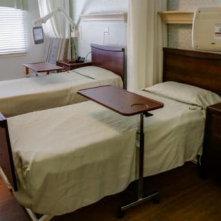A hospital room with two neatly made beds and overbed tables.