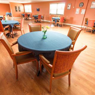 A cozy dining area featuring a round table with a blue tablecloth and chairs, set against an inviting orange wall.