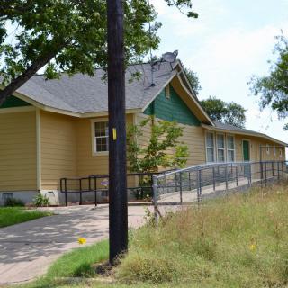 A yellow house with a ramp and surrounding trees.