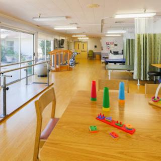 A spacious and well-lit activity room in a rehabilitation center, featuring colorful toys and therapy equipment.