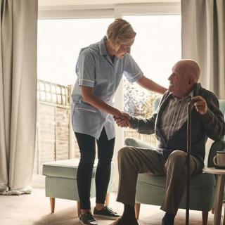 A caregiver assisting an elderly man in a living room setting.