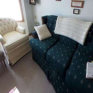 A cozy living room featuring a patterned sofa with cushions and an armchair, complemented by framed pictures on the wall.