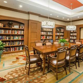A cozy library with a conference table surrounded by bookshelves and elegant lighting.