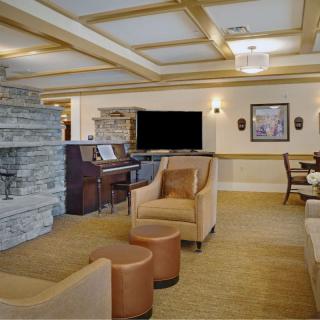 A cozy living room with comfortable seating, a piano, and a television, featuring a stone wall and elegant ceiling lighting.