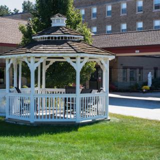 A white gazebo situated on a lawn in front of a large brick building.