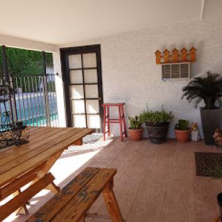A cozy outdoor patio with a wooden dining set, surrounded by potted plants and bathed in sunlight.