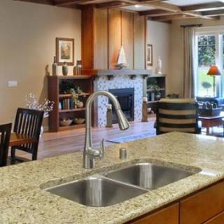 A modern kitchen with a double sink and granite countertop, overlooking an open living room.