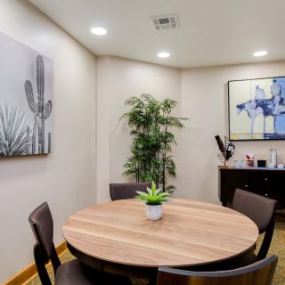 A small meeting room with a round table, four chairs, and decorative plants and artwork.