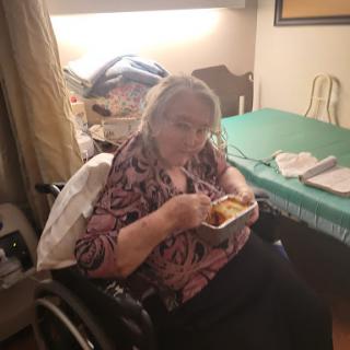 An elderly woman enjoying a meal while seated in her wheelchair.