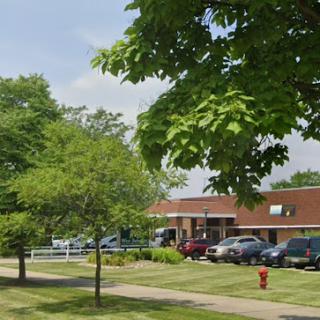 A view of a commercial building surrounded by trees and parked cars on a sunny day.