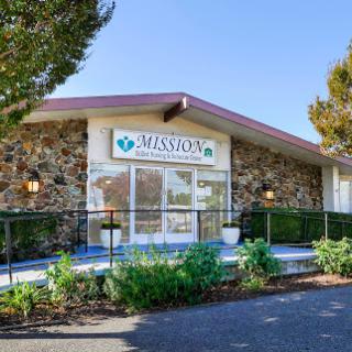 A welcoming entrance to a facility with a stone facade and lush landscaping.