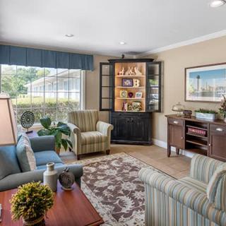 A cozy living room with comfortable seating, decorative shelves, and natural light from a large window.