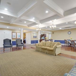 Spacious living room with elegant furnishings, including a sofa and chairs, under a coffered ceiling with chandeliers.