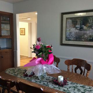 A dining room with a wooden table and chairs, adorned with a bouquet of flowers and a painting on the wall.