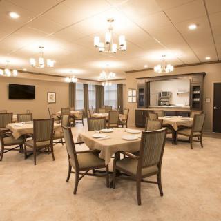 An elegant dining room with neatly arranged tables and chairs, illuminated by chandeliers.
