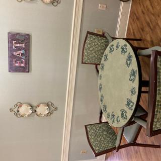A cozy dining area with an oval table and patterned chairs, complemented by decorative wall accents and a sign that reads 'EAT'.