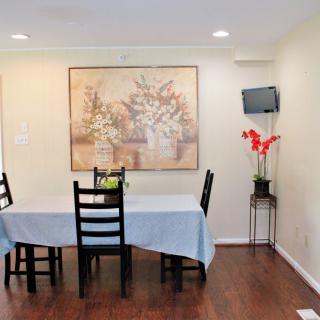 A cozy dining room with a table set, wall art, and a small television mounted beside a flower vase.