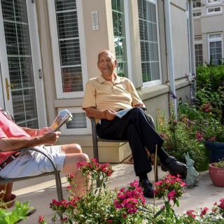Two people sitting and talking in a garden patio surrounded by plants.