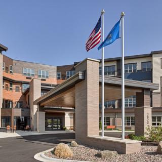 A modern building entrance with American and blue flags flying high on a clear day.