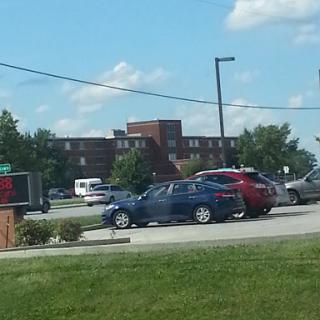 A view of a parking lot with several cars and a building in the background under a clear blue sky.