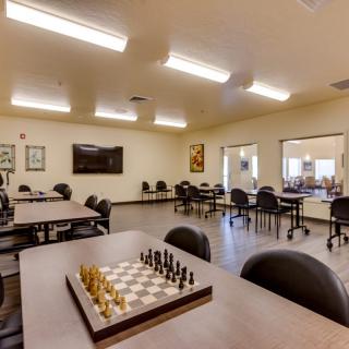 A classroom setting featuring tables and chairs, with a chess board set up in the foreground.