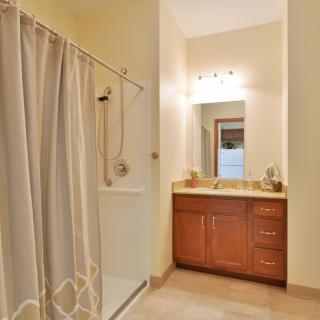 A clean and well-lit bathroom featuring a shower with a curtain, vanity sink area, and a mirror.