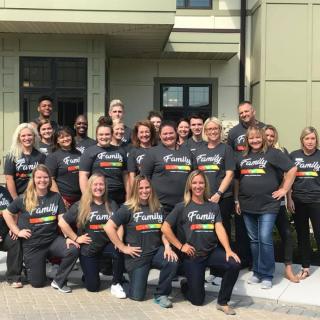 A group of people wearing matching t-shirts posing for a team photo outside a building.