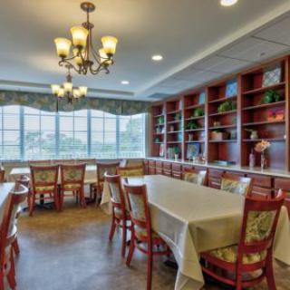 A spacious dining room with elegant chandeliers, lined with bookshelves and large windows, featuring neatly arranged tables and chairs.