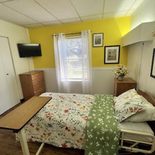 A cozy hospital room featuring a neatly made bed, a television, and warm yellow walls, creating a welcoming atmosphere.