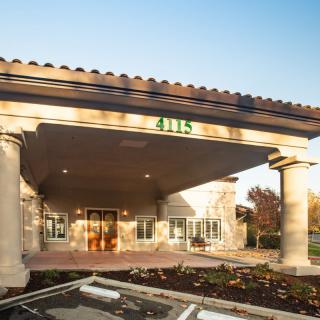 A view of a building entrance with columns and landscaped surroundings.