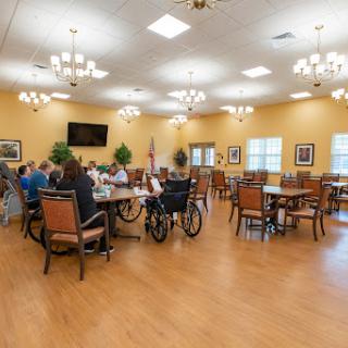 A spacious dining area in a community center, filled with elderly residents engaged in conversation.