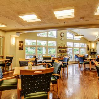 A cozy and well-lit cafe interior with wooden floors, tables, and chairs.