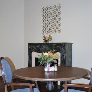 A cozy dining room with a round table and chairs, featuring floral decorations on the fireplace.