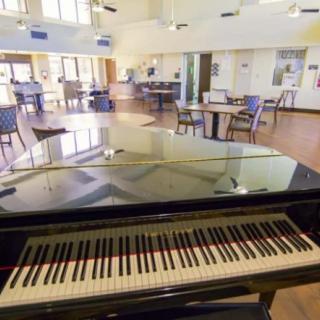 A grand piano in a spacious music room with tables and chairs.