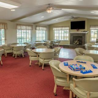A spacious community room with tables and chairs set up for games, featuring large windows and a television.