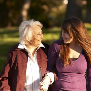 An elderly woman and a young woman walking hand in hand in the park.