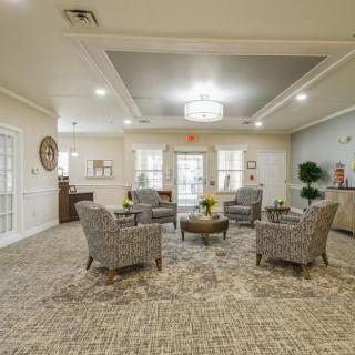 A spacious and elegantly designed lobby area featuring a central seating arrangement with patterned chairs and a modern lighting fixture.