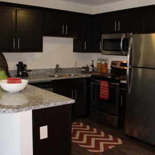 A modern kitchen with dark cabinets and stainless steel appliances.