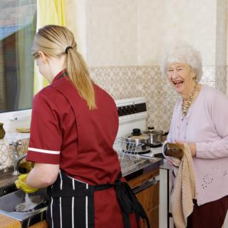 A caregiver assists an elderly woman in the kitchen.